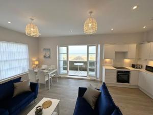 Una sala de estar con un sofá azul y una cocina. en Beachfront Bliss Apartment - Near Hythe - On Beach Seafront - Private Parking, en Dymchurch