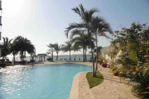 una gran piscina con palmeras y el océano en Apartamento - Resort Bunsichari, en Santa Marta