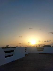 un coucher de soleil sur une clôture blanche avec le soleil dans le ciel dans l'établissement Magnifique appartement djerbien, à El Guecheïne