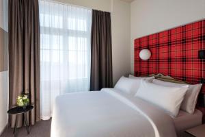 a bedroom with a large white bed and a red wall at NH Bern The Bristol in Bern