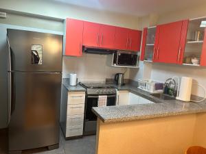 eine Küche mit roten Schränken und einem Kühlschrank aus Edelstahl in der Unterkunft Acogedor apartamento centrico, tranquilo con piscina in Lima