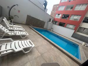 a hotel with a pool and lounge chairs next to a building at Acogedor apartamento centrico, tranquilo con piscina in Lima