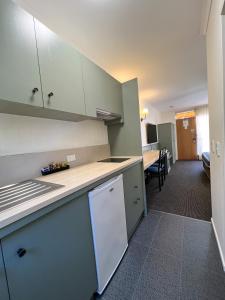una cocina con armarios blancos y una mesa en una habitación en Summerhill Motor Inn, en Merimbula