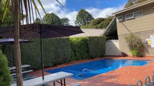 uma piscina com um guarda-sol em frente a uma casa em Barrass's John Bright Motor Inn em Bright