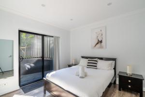 a white bedroom with a bed and a window at Sunrise on Easts 1 in Kiama