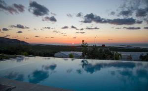 a large swimming pool with a sunset in the background at Petras Resort in Falasarna