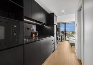 a kitchen with black cabinets and a view of a bedroom at Rambla at South City SQ in Brisbane