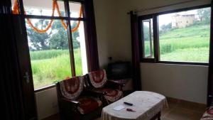 a room with two chairs and a table and windows at Yog Homestay in Chaubattia +4 photos