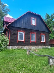 a wooden house with red windows in the grass at Zirgu sēta "Klajumi" - Horse ranch "Klajumi" in Kaplava