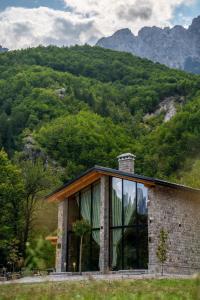 uma casa de pedra com uma grande janela em frente a uma montanha em Villa Ujëvara e vogël em Theth