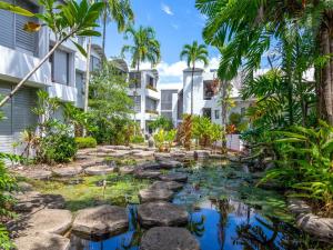 einen Koi-Teich in einem Garten mit Palmen und Gebäuden in der Unterkunft Portside Studio in Port Douglas
