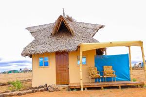 a small house with a thatched roof and two chairs at Amanya Zebra 1-Bed Wigwam in Amboseli in Amboseli