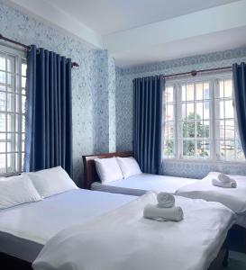 Dos camas en una habitación con paredes y ventanas azules. en Glory Gia Huy Hotel, en Da Lat