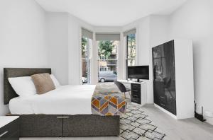 a white bedroom with a bed and a television at Hackney Suites in London
