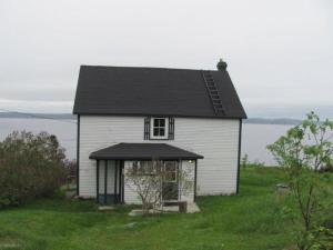 a white house with a black roof on top of a field at Wolf Cove Retreat House in Amherst Cove