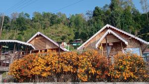 un grupo de cabañas de madera con flores delante de ellas en Kapchakays Farmstay by StayApart, en Kalimpong