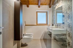 een badkamer met een toilet, 2 wastafels en een raam bij Appartamento Midum Domus Attic in Trento