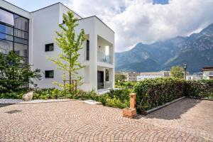 een wit gebouw met een boom en bergen op de achtergrond bij Appartamento Midum Domus Attic in Trento