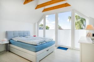 a white bedroom with a blue bed and windows at Haus am See, exquisites Relaxen in Südbrookmerland