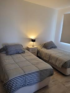1 dormitorio con 2 camas y mesita de noche con lámpara en departamento temporario en Esquel