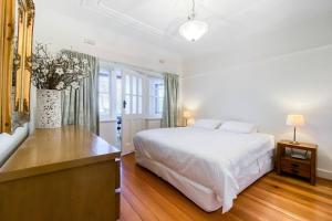 a white bedroom with a large bed and a vase with flowers at 'The Gables' Stylish Victorian Beachfront Abode in Melbourne