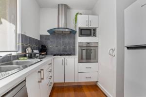 a white kitchen with white cabinets and a sink at Enjoy The Esplanade's Treats From Acland Street in Melbourne