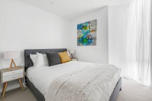 a white bedroom with a bed and a painting on the wall at The Nest on Nott - Pure Port Melbourne Bliss in Melbourne