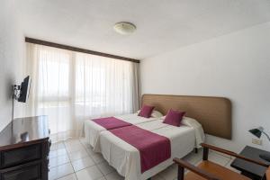 1 dormitorio con 1 cama grande con almohadas moradas en Apartamentos Borinquen, en Playa de las Américas