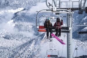 dos personas sentadas en un remonte con una tabla de snowboard en Comtes d’Urgell en Andorra la Vella