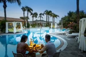 a man and woman sitting at a table by a pool at Cruccùris Resort - Adults Only in Villasimius