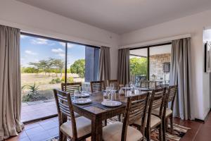 jadalnia ze stołem i krzesłami oraz dużymi oknami w obiekcie Ol Pejeta Mansion w mieście Nanyuki