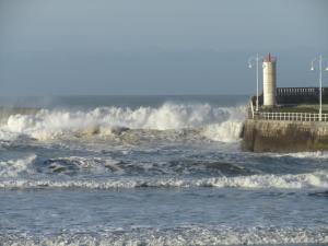 a beach with waves and a lighthouse in the ocean at Marina in Ribadesella