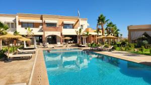 a swimming pool with chairs and umbrellas next to a building at Hôtel Jardins de lina et lea in Marrakesh