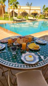 馬拉喀什的住宿－Hôtel Jardins de lina et lea，一张桌子,上面有早餐食品,放在游泳池前