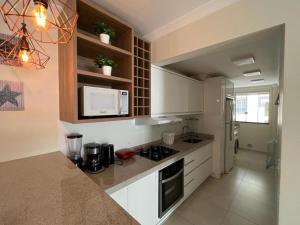 Apartamento Novo Praia de Bombas في بومبينهاس: مطبخ فيه دواليب بيضاء وثلاجة بيضاء