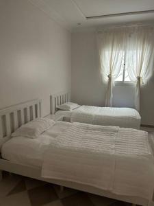 two beds in a white bedroom with a window at Riyadh, King Faisal District Apartment in Riyadh