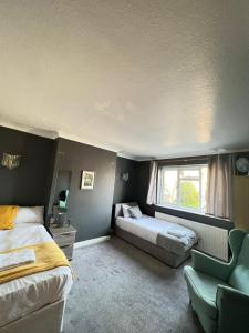 a bedroom with two beds and a chair and a window at Airport Garden Rooms in Feltham