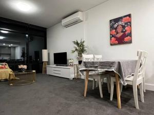 uma sala de estar com uma mesa e cadeiras e uma televisão em Lovely 2 bedroom APT in centre of Olympic Park em Sydney