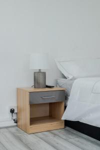 1 cama con mesita de noche de madera junto a la cama en Floral, 5 Bed House in London with Garden, Parking en Dagenham