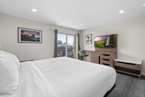 a white bedroom with a bed and a tv at Cedar Street Hotel & Suites in Sandpoint