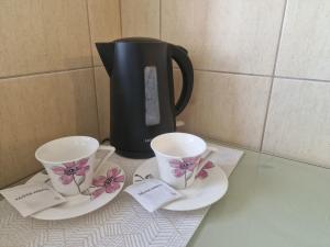 twee kopjes en schotels op een aanrecht met een koffiepot bij Butas 34 in Šiauliai