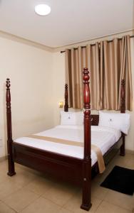 a bedroom with a wooden bed with white sheets at Ubuntu Palace Hotel in Kampala
