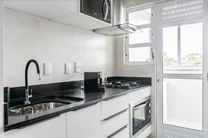 a kitchen with white cabinets and a sink and a window at Prédio com apartamentos completos, com piscina e a passos da praia - Agua Marinha in Florianópolis