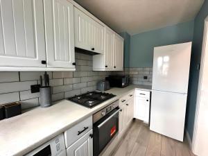 cocina con armarios blancos, fogones y nevera en New Stylish 2 Bedroom House, en Kent