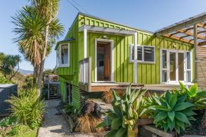 a green tiny house with a porch and palm trees at Karioi View in Raglan