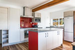 uma cozinha com armários brancos e uma ilha vermelha em Karioi View em Raglan