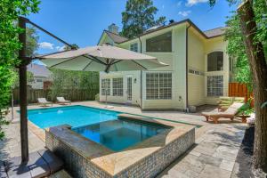 a swimming pool with an umbrella in front of a house at Woodlands Contemporary 4BR3Bath with heated Pool and Spa in The Woodlands