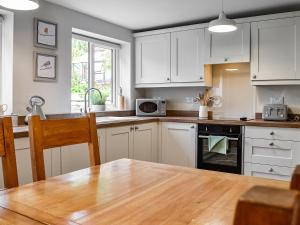 a kitchen with white cabinets and a wooden table at Southways Cottage in Cumwhinton
