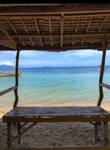 a wooden bench sitting on a beach with the ocean at Beach Front Calatagan Apartelle in Calatagan
