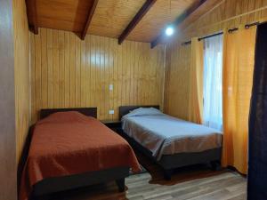Duas camas num quarto com paredes de madeira e uma janela em CABAÑAS 88 Y 8 em Coñaripe